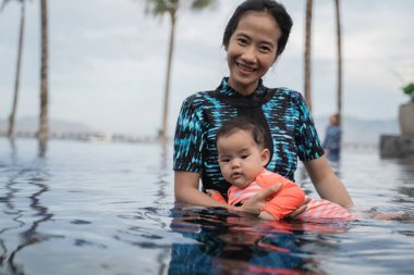 Anne havuzda yüzerken çocuğunu tutuyor.