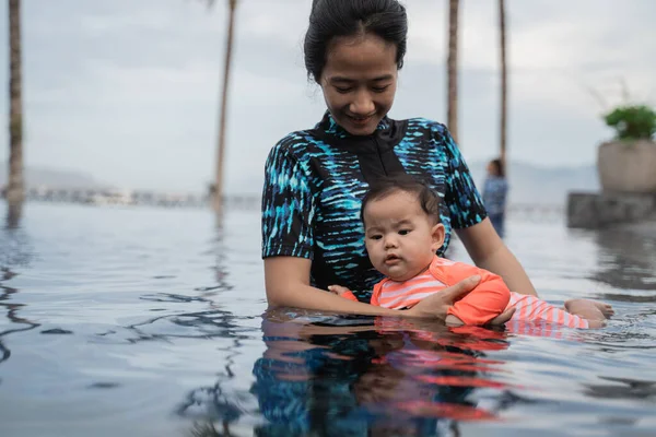 Anne yüzme öğrenirken bebeğini kucağında tutuyor. — Stok fotoğraf