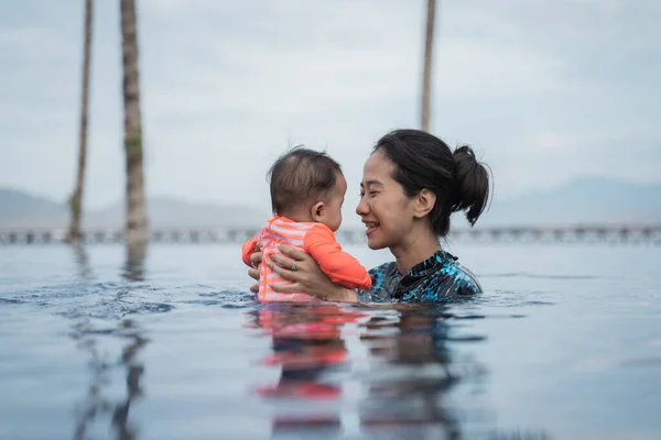 プールで泳いでいる間に子供を抱いている母親は — ストック写真