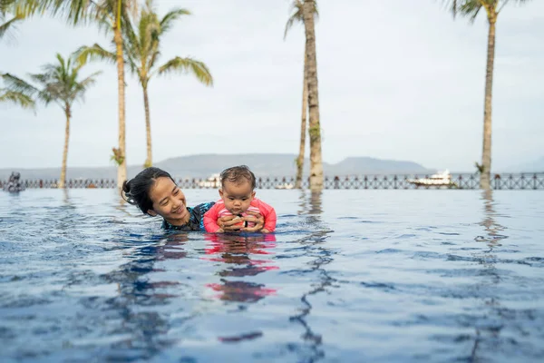Asiatisk mor holder sin lille baby mens hun svømmer - Stock-foto