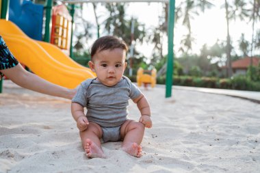Kumda otururken annesinin kucağına aldığı bebek.
