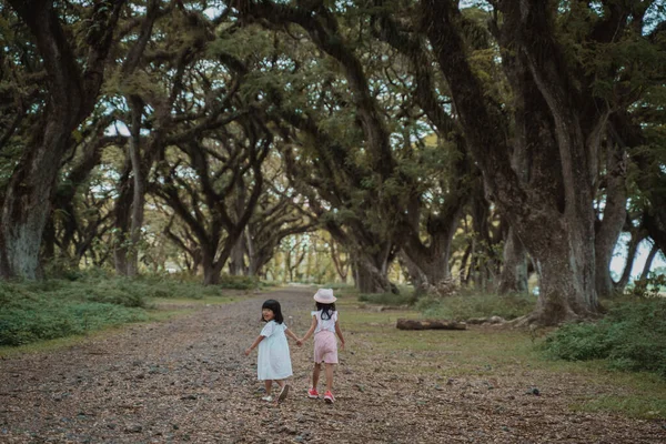 Två barn går iväg mellan ett skumt träd — Stockfoto