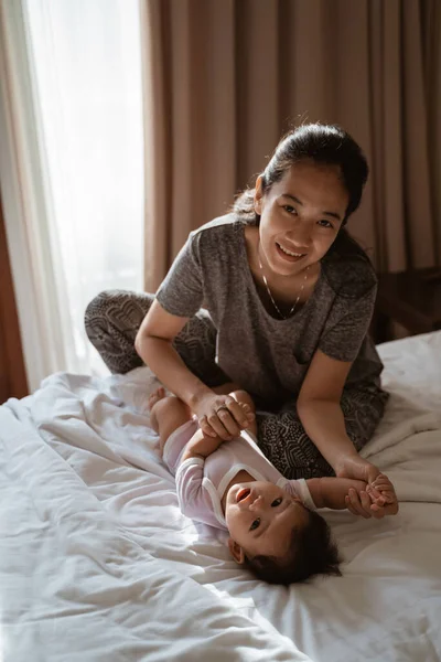 Ásia mãe segurando um pouco filha mãos no o cama — Fotografia de Stock