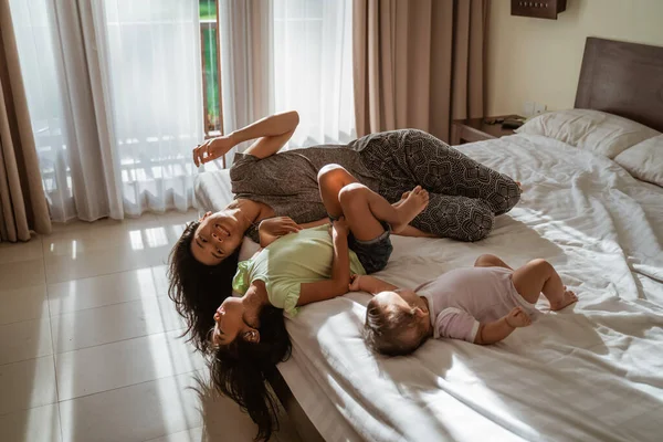 İki küçük kız, anneleri yanlarındayken yatakta yatıyorlar.