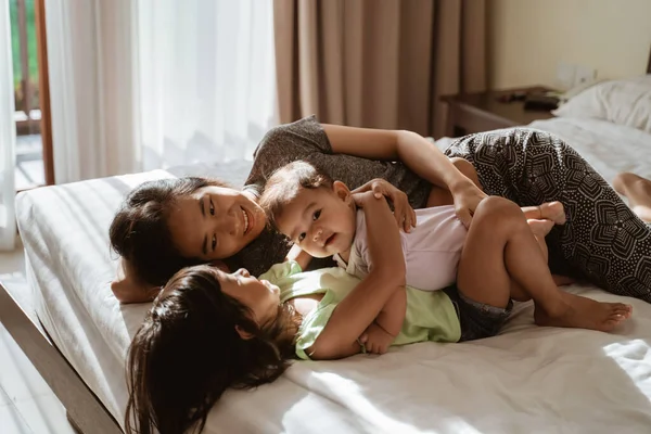 Dvě dcerušky ležící v posteli se svou matkou vedle nich — Stock fotografie