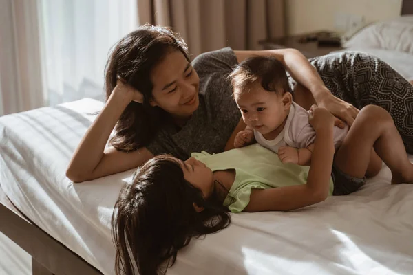隣の母親とベッドに寝そべっているアジア系の子供たち — ストック写真