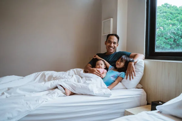 Padre joven y sus dos hijos se sientan en la cama — Foto de Stock