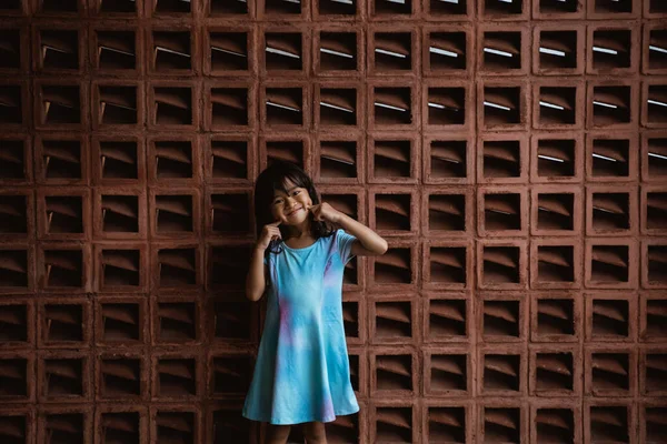 Niña está de pie con su gesto de mano sosteniendo su mejilla frente a la pared —  Fotos de Stock