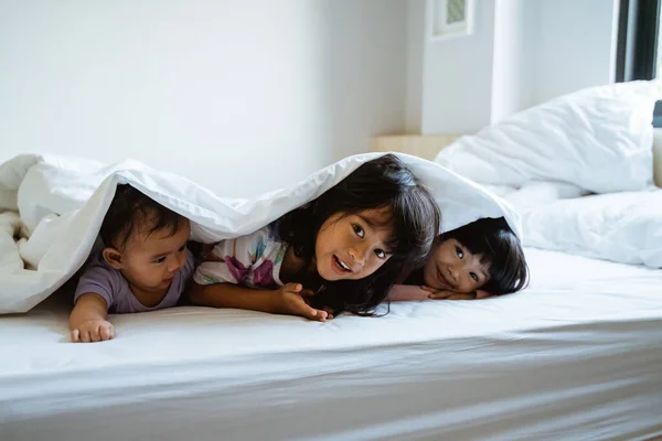 Tre barn leker och gömmer sig under täcket — Stockfoto