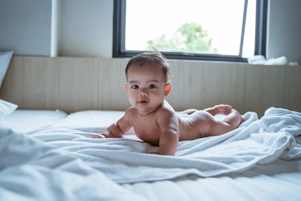 Bebé propenso desnudo es sonrisa mientras está acostado en la cama —  Fotos de Stock
