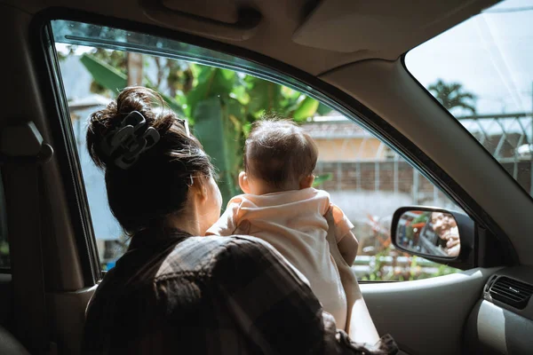 母親が赤ん坊を抱えて車の窓から外を見ると — ストック写真