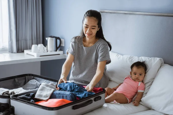 Bebê se senta ao lado da mãe preparando roupas — Fotografia de Stock