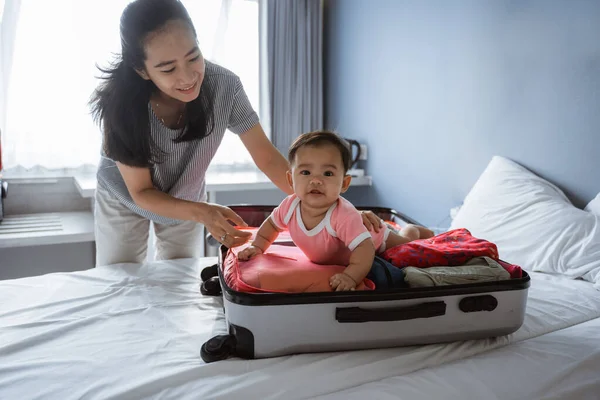 Mamá sonríe sosteniendo a un lindo bebé acostado en una maleta abierta llena — Foto de Stock