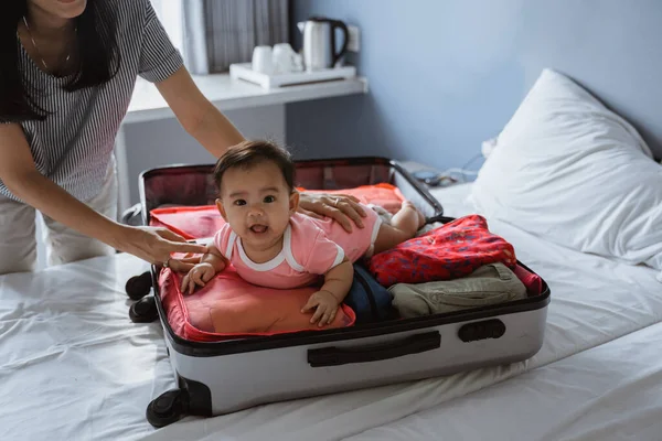 Ásia mãe sorrisos segurando um bonito bebê deitado no um aberto mala preenchida — Fotografia de Stock