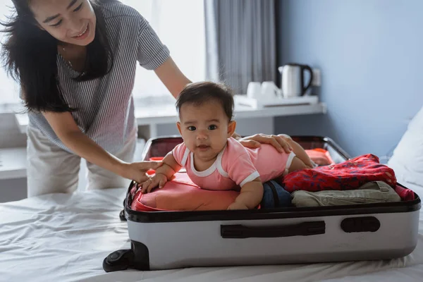 Anya mosolyog, kezében egy aranyos baba fekszik egy nyitott bőröndben tele — Stock Fotó