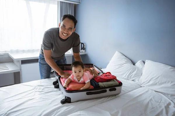 Азіатський батько посміхається, тримаючи гарну дитину лежачу у відкритій валізі, дивлячись на камеру. — стокове фото