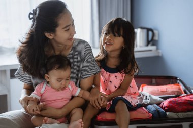 Anne valizi hazırladıktan sonra iki çocuğuyla sohbet ediyor.