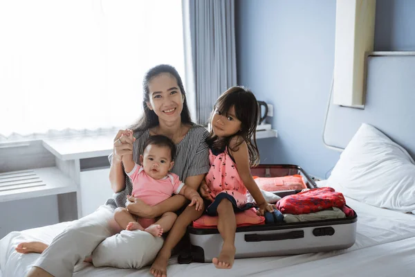 Мать и двое ее детей улыбаются сидя на кровати — стоковое фото