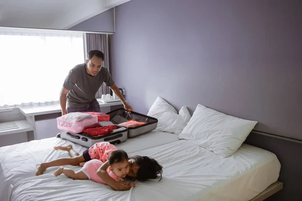 两个孩子在床上玩耍时，亚洲父亲正在准备手提箱 — 图库照片