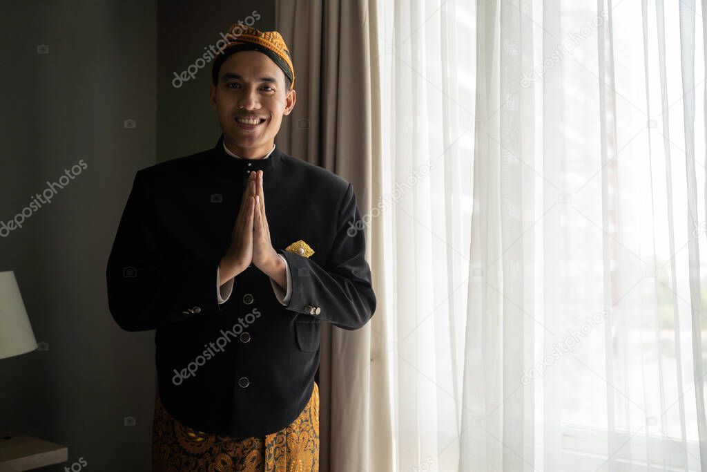 Asian man wearing traditional clothes of indonesian beskap with welcome gesture