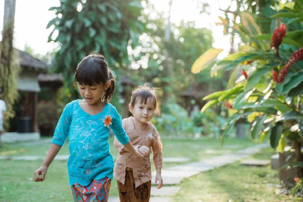 Duas menina bonita vestindo kebaya javanês tradicional com as mãos dadas quando caminhando juntos — Fotografia de Stock