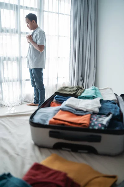 Jovem asiático homem usa uma camisa depois de abrir sua mala no quarto — Fotografia de Stock