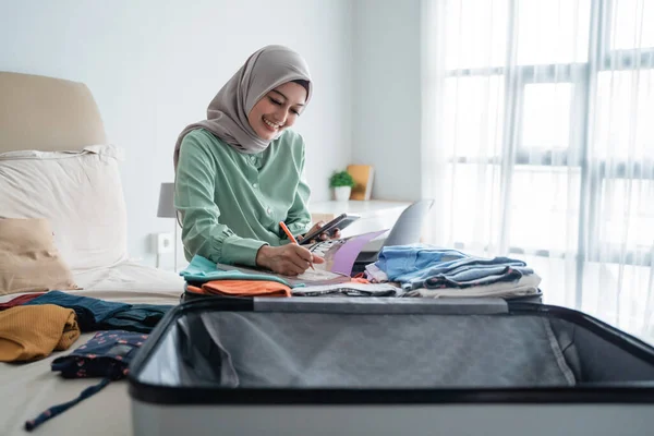 veiled woman sitting on the bed while looking at the list of items