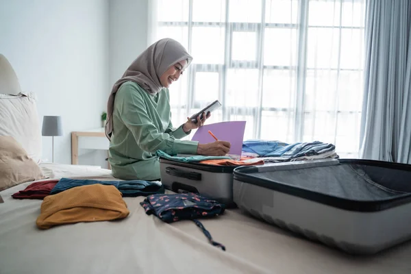 Hijab mulher sentada na cama enquanto olha para a lista de itens — Fotografia de Stock