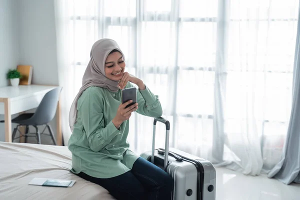 Jong aziatisch vrouw zitten op het bed met haar handtelefoon en koffer — Stockfoto