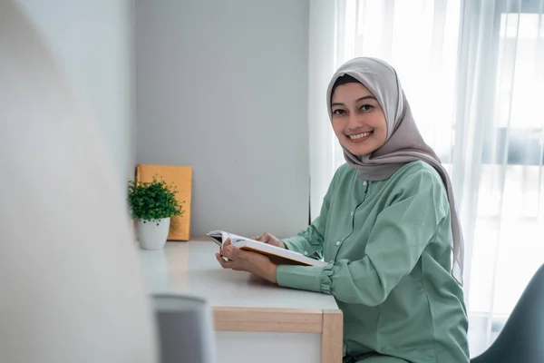 Hermosa joven vistiendo un hijab sonriendo sosteniendo el libro sagrado del Corán —  Fotos de Stock