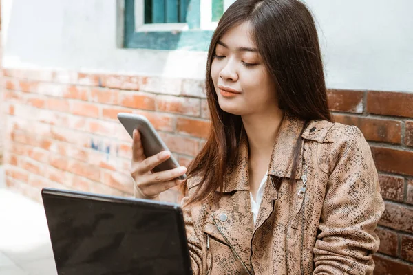 Donna che lavora con il computer portatile e il suo telefono cellulare — Foto Stock