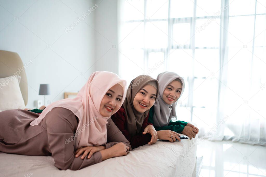 Asian hijab woman with friends lying on the bed enjoy watching the television