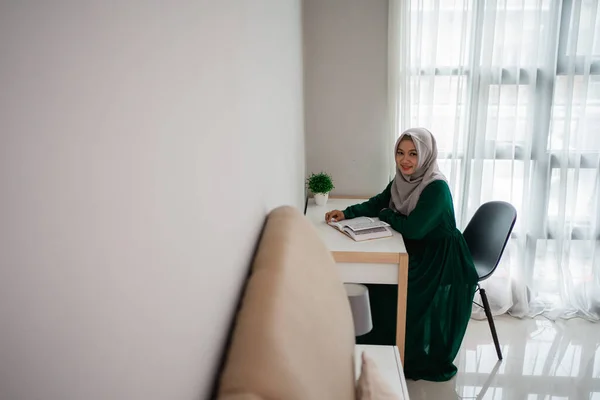 Asijské hidžáb ženy s úsměvem, když sedí na židli studovat a číst svatou knihu Al-quran — Stock fotografie