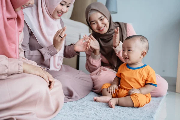Ibu muslim asia dengan teman-temannya menikmati bermain dengan anaknya ketika duduk di lantai — Stok Foto