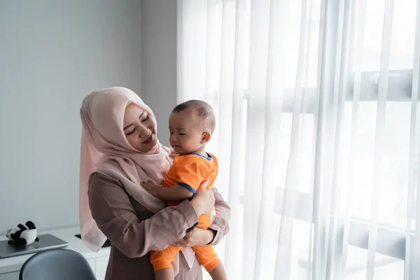 Asian moslem mother carrying her little boy when playing near window — Stock Photo, Image