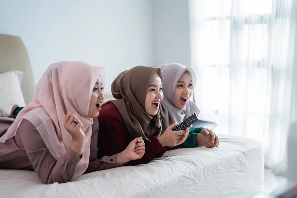 Tiga wanita terselubung berbaring di tempat tidur menikmati menonton tv — Stok Foto