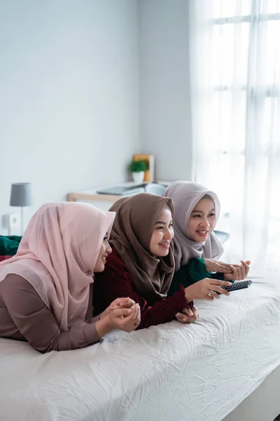 Arkadaşlarıyla yatakta uzanan Asyalı tesettürlü kadın televizyon izlemenin tadını çıkarıyor. — Stok fotoğraf