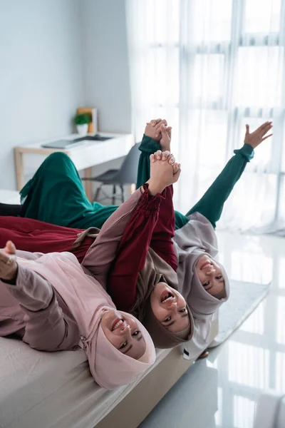 Perempuan dan teman-teman hijab asia berbaring dan mengangkat tangan di tempat tidur sambil bersenang-senang bersama — Stok Foto