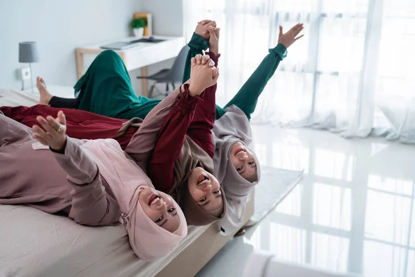 Tres mujeres veladas se tumban y las manos levantadas en la cama mientras se divierten juntas —  Fotos de Stock