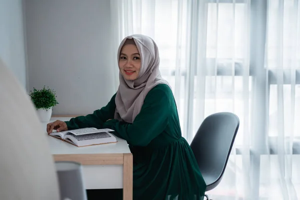 Wanita hijab asia tersenyum ketika duduk di kursi belajar dan membaca kitab suci Al-quran — Stok Foto