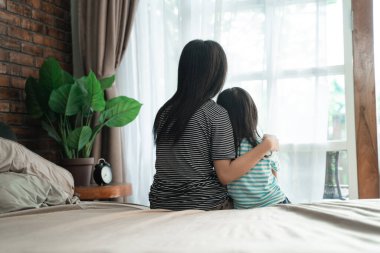 Kardeş yatakta oturup pencereye bakıyor.