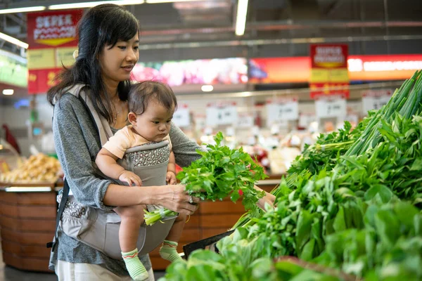Asiatin trägt ihr Baby beim Einkaufen — Stockfoto