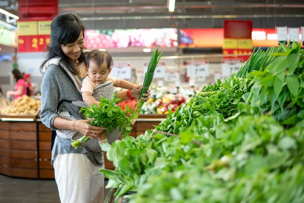 Alışveriş yaparken bebeğini taşıyan Asyalı kadın. — Stok fotoğraf
