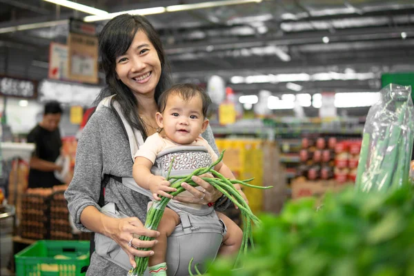 Asiatin trägt ihr Baby beim Einkaufen — Stockfoto