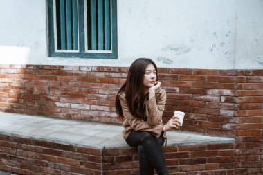 Kadın yol kenarında oturup bir fincan kahvenin tadını çıkarıyor.