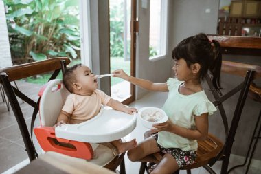 Küçük kız kardeşini besleyen kardeşi.