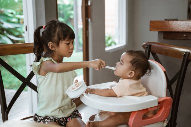 Küçük kız kardeşini besleyen kardeşi.