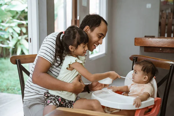 Father and daughter feeding her baby sister — Stock Photo, Image