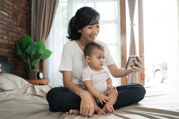 Moeder met behulp van mobiele telefoon met haar baby — Stockfoto