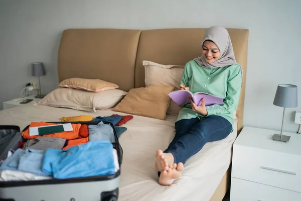 Hijab-Frau sitzt auf dem Bett, während sie sich die Liste der Gegenstände ansieht — Stockfoto